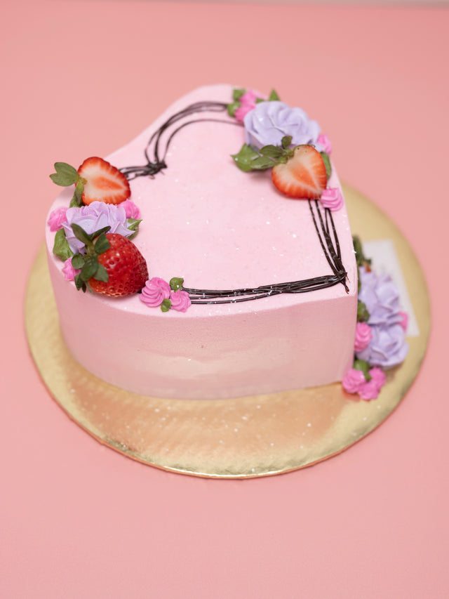 Heart-shaped pink cake with floral decorations and strawberries on a pink background