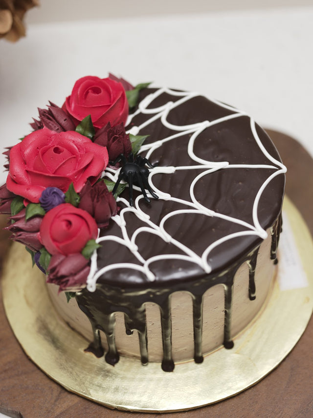 Chocolate drip Halloween cake with a white spider web and red roses