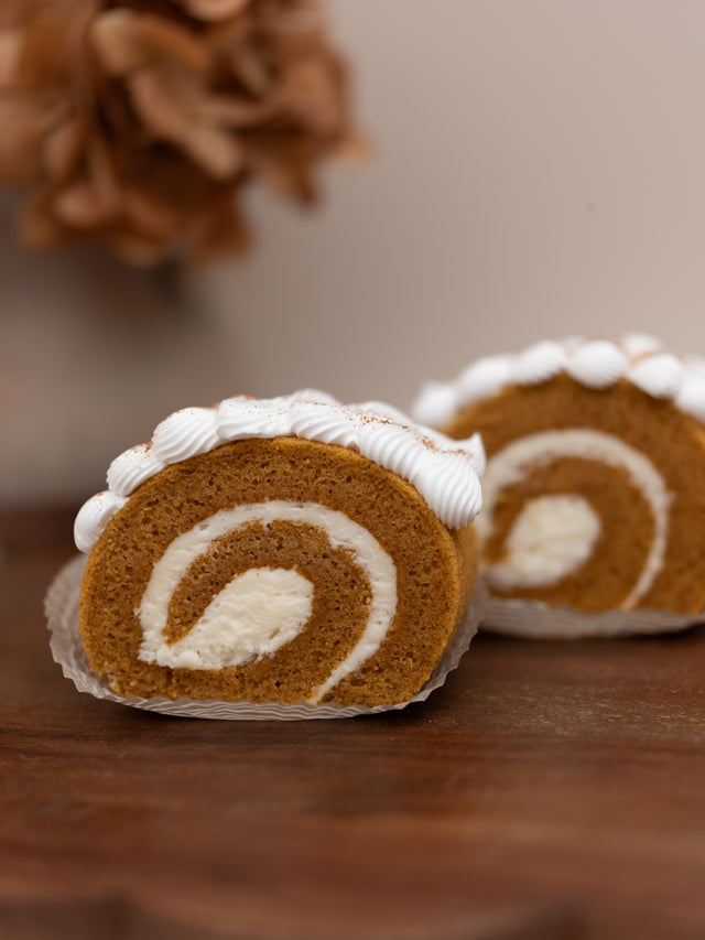 A close-up of a pumpkin spice cake roll with white cream swirl and piped frosting on top.